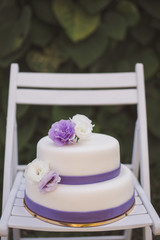 White wedding cake with purple decoration outdoors on white wooden chair
