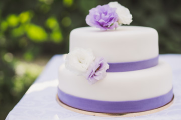 White wedding cake with purple decoration outdoors on the table