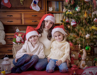 Children sitting with mother under Christmas tree in hats