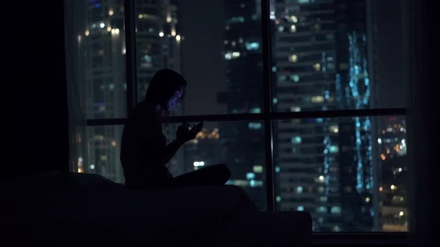 Young, Pretty Woman Using Smartphone Sitting On Bed At Night, 4K

