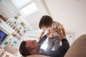 Cheerful young boy having fun with father on sofa