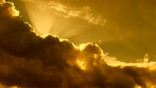 Beautiful cloudscape with large, building clouds and sunset behind shining sun rays and eventually breaking through cloud mass.