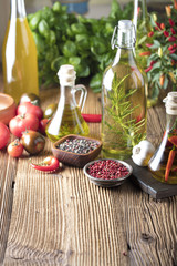 Olive oil and rosemary, chili pepper, many different tomatoes, garlic, red, white, green pepper on old wooden table. Extra virgin olive oil cruets and flavored olive oils with rosemary and chili.