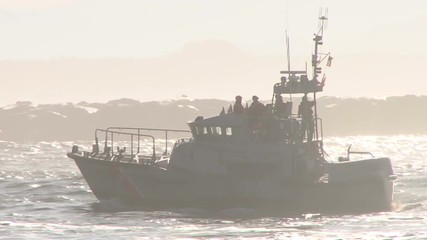 United States Coast Guard speeding through harbor waters in the Pacific Northwest coastline on sunny day.