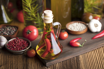 Olive oil and rosemary, chili pepper, many different tomatoes, garlic, red, white, green pepper on old wooden table. Extra virgin olive oil cruets and flavored olive oils with rosemary and chili.
