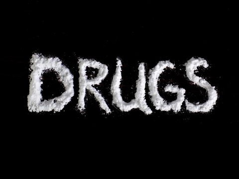 Cocaine drug powder in drugs word shaped on black background