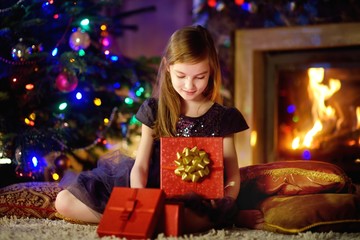 Fototapeta na wymiar Happy girl opening Christmas gifts by a fireplace