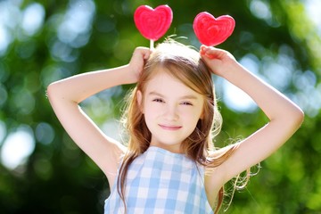 Cute little girl eating huge heart-shaped lollipops outdoors © MNStudio