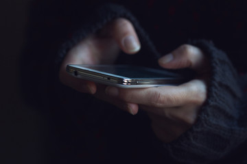 Close up of woman in dark sweater hands holding a phone