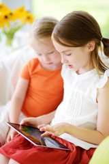 Two adorable little sisters playing with a digital tablet