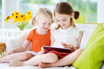 Two adorable little sisters playing with a digital tablet