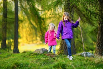 Two funny little sisters having fun during forest hike on beautiful autumn day
