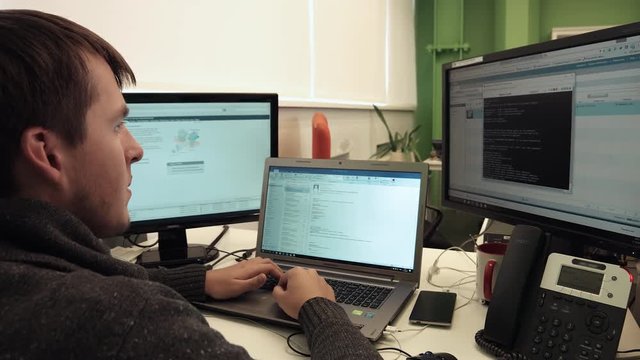 Operator of Helpdesk Sits in Front of Three Monitors