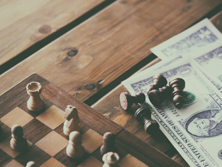 Chess figures and US dollars on wooden chessboard with selective focus and retro color, business strategy planning