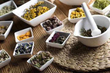 Herbs, berries and flowers with mortar, on wooden table background