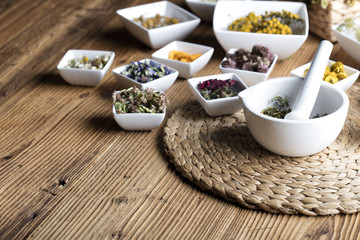 Herbs, berries and flowers with mortar, on wooden table background