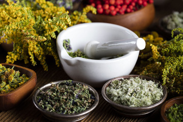 Herbs, berries and flowers with mortar, on wooden table background