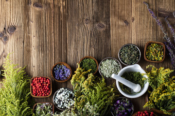 Herbs, berries and flowers with mortar, on wooden table background