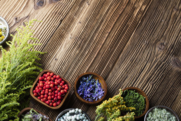 Herbs, berries and flowers with mortar, on wooden table background