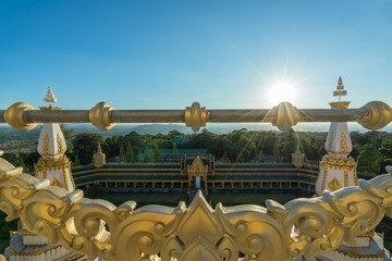 Temple scene : beautiful Golden handrails frame in front a White and gold pagoda with sunbeam light blue sky at Maha Chedi Mongkhol temple, Roi Et, Thailand.

