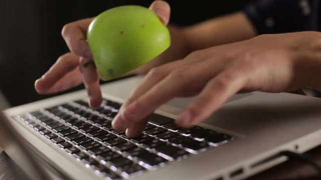 male hands holding green apple and typing on keyboard laptop