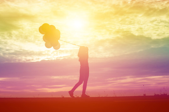 silhouette of young woman holding colorful of balloons with suns