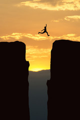 Man jump through the gap between hill.man jumping over cliff on sunset background,Business concept...