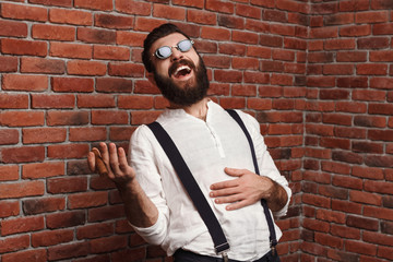 Young handsome man laughing holding cigar over brick background.