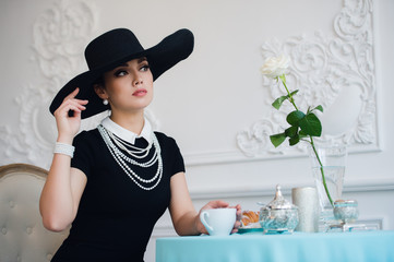 Woman in hat, much like the famous actress, croissant eating and drinking tea.