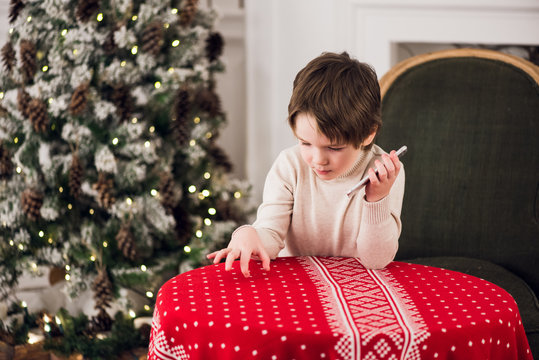 boy calls Santa while sitting on a big green armchair at home over chirstmas tree background