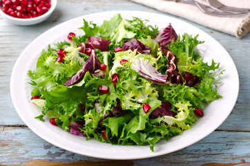 Green salad with spinach, frisee, arugula, radicchio and pomegranate seeds on blue wooden background