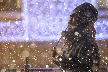 Girl walking in a winter city. The buildings are decorated with Christmas lights. Snowfall, evening, dark. Copy space.