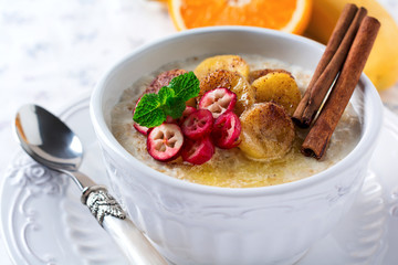 Oat porridge with baked bananas, cinnamon,orange and cranberries in a ceramic bowl for healthy...