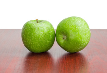 Two green apples on a red wooden surface
