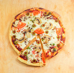 Partly sliced cooked pizza with chicken, mushrooms, tomatoes and olives