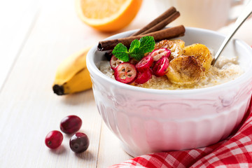 Oat porridge with baked bananas, cinnamon,orange and cranberries in a ceramic bowl for healthy breakfast on a light background. Selective focus.