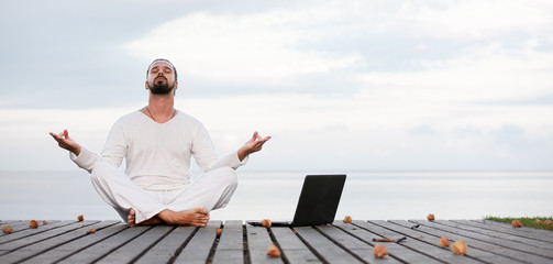 Fototapeta na wymiar Man in white clothes meditating yoga with laptop on wooden pier