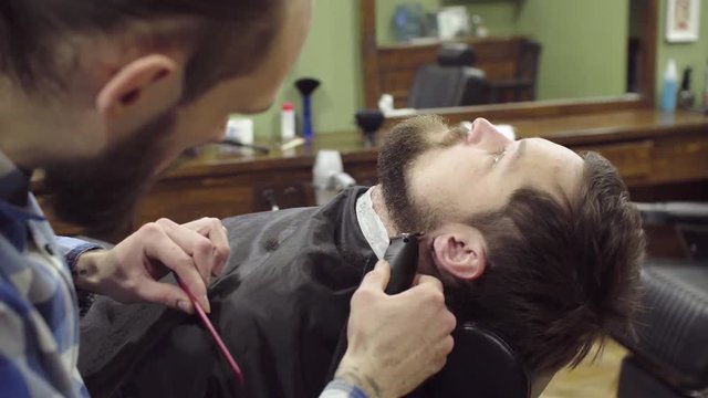Barber woman trimming beard of client with clipper at barbershop