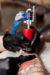 Master tattoo draws the orange paint on the clients tattoo. Tattoo artist holding a pink tattoo machine in black sterile gloves
