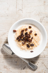 Bowl of Porridge Oats and raisins on White Wooden Background