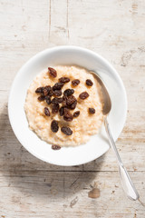Bowl of Oatmeal and sultanas on White Wooden Background