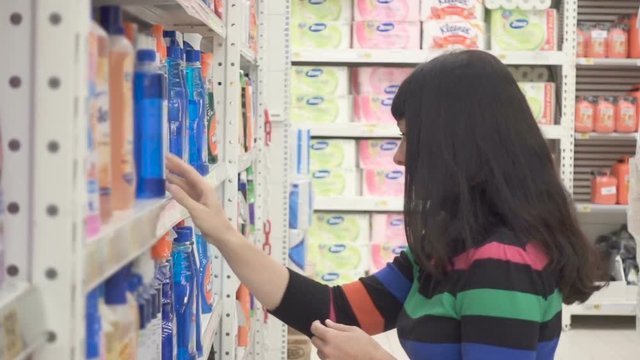 Young woman choosing household detergents in the section of home care in the supermarket. Great assortment on the shelves