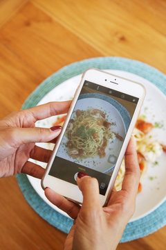 Woman taking photo of spaghetti with smartphone
