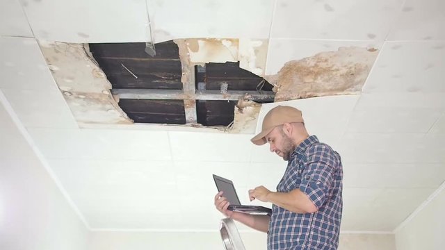 young man makes an emergency inspection of ceiling and use laptop PC. public utilities. Ceiling panels damaged huge hole in roof from rainwater leakage.Water damaged ceiling , Insurance agent.