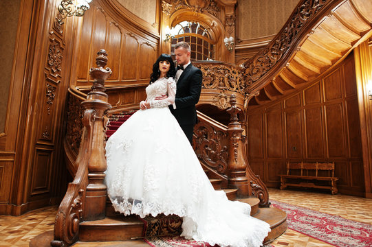Amazing wedding couple on big wooden stairs at rich palace.