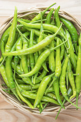 Green peppers in wicker basket on wooden background