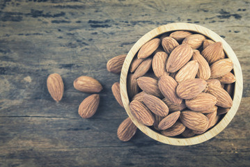 Almonds in brown bowl on textured wooden background, top view. Copy space on left side. Almond vintage tone