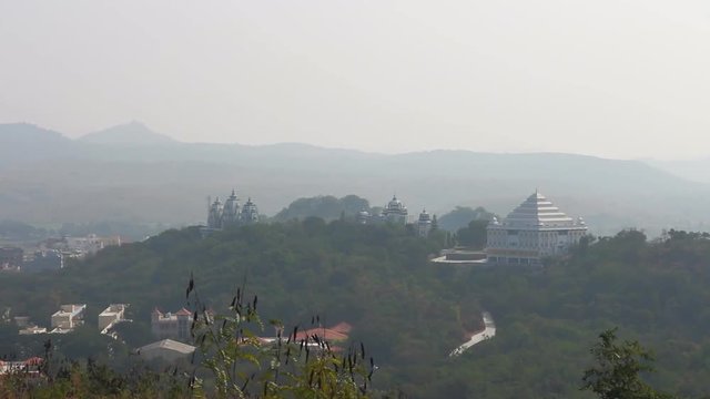 Romantic India: green hills, matinee misty distance, Hindu temple (pagoda, Mandir, mausoleum), pagodas and pods of acacia swaying in front of lens. Relief birds eye view
