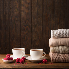 Two cups of hot tea, strawberry chocolate candies and Stack of cozy knitted sweaters on rustic dark wooden background. Valentine's day celebration concept. Winter time