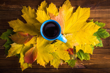 Autumn leaves, hot steaming cup of coffee on wooden table background